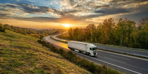 Camion blanc circulant sur l'autoroute en asphalte dans un paysage d'automne au coucher du soleil doré avec des nuages spectaculaires